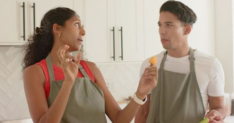 Couple tasting homemade bite in bright modern kitchen wearing olive aprons and smiling