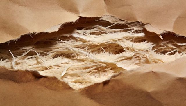 Torn kraft paper revealing pale textured packing fibers macro background for sustainable packaging