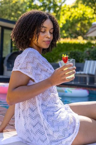 African american woman relaxing poolside in white coverup holding drink with strawberry