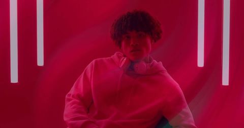 Man relaxing in hoodie with headphones amid neon glow