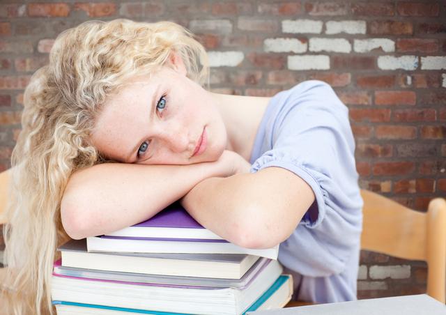 Tired Teenage Girl Resting on Stack of Books Against Brick Wall - Download Free Stock Photos Pikwizard.com