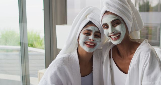 Image of happy diverse female friends moisturizing with face masks in bathroom. Friendship and taking care of yourself and beauty concept.