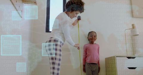 Caregiver measuring child height at home with tape measure marking growth on wall
