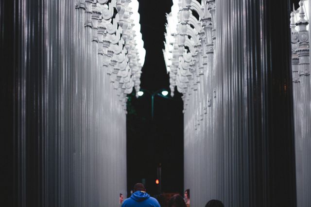 Captured at night, people walk through a stunning urban light installation consisting of numerous tall, illuminated columns. Perfect for articles on city attractions, modern art, or night photography. Suitable for use in travel brochures, blog posts on public art, or social media posts highlighting urban exploration.
