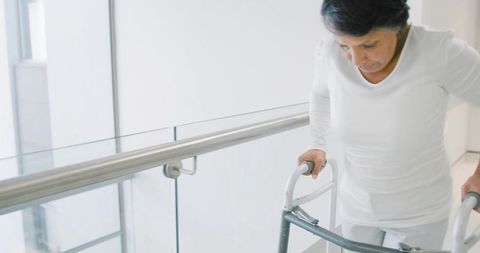 Mature woman walking with rolling walker in bright healthcare corridor promoting mobility
