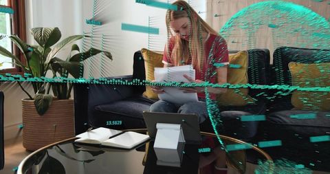 Young woman reviewing paperwork on sofa with tablet and notebook, remote work lifestyle