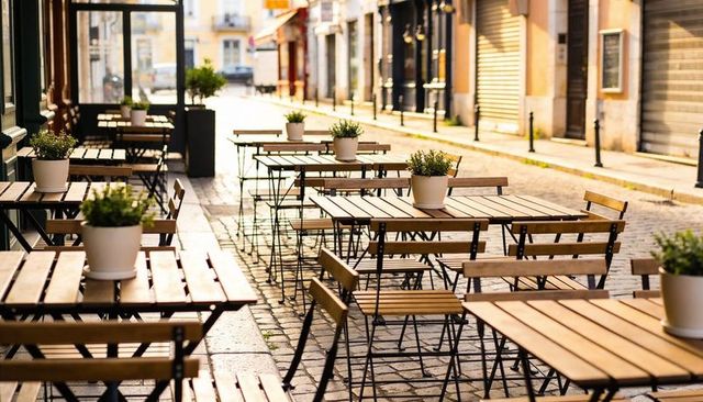 Sunlit european café terrace with wooden tables and folding chairs on cobblestone street