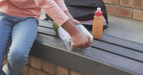 Girl enjoying lunch break on school bench with box and juice