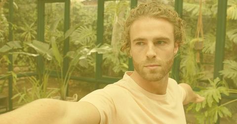 Man standing in greenhouse reaching toward tropical plants exploring sunlit conservatory