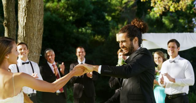 A bride and groom are joyfully holding hands during their wedding ceremony outdoors, surrounded by guests. The image captures a moment of happiness and celebration, with friends and family sharing in the couple's special day.
