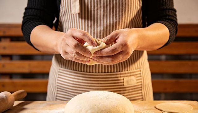 Female hands shaping dough and forming bun over floured board with striped apron