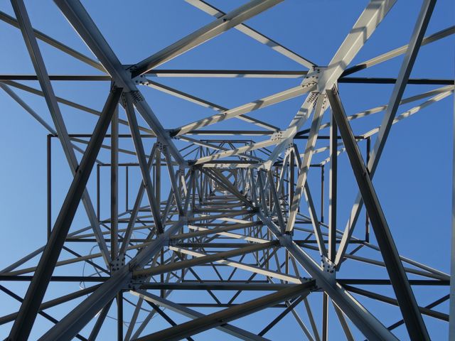 Interior perspective of metal tower with intricate lattice structure and clear blue sky provides an impressive representation of industrial design and structural engineering. Suitable for use in articles about construction, engineering marvels or modern architecture designs. Useful for educational materials, promotional constructions, infrastructure projects, and more.