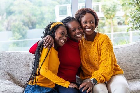 African american mother embracing smiling teen daughters on sofa cozy home moment