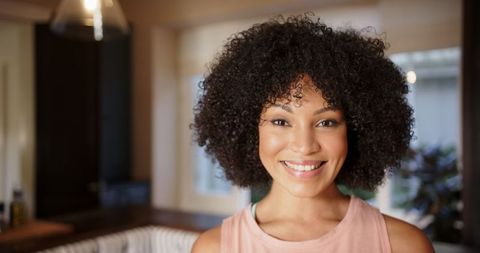 Smiling woman with curly hair indoors embracing joyful lifestyle