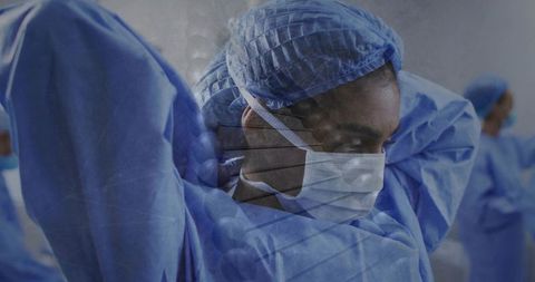 Mid-adult clinician adjusting surgical gown and mask during sterile operating room prep