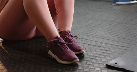 African american woman 30s resting on rubber gym floor in pink leggings and purple sneakers