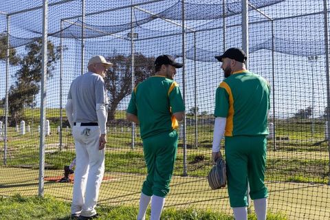 Coach guiding two green-uniform players during net practice on sunny field