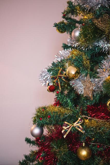 This image captures a close-up view of a beautifully decorated Christmas tree at home. The tree is adorned with various ornaments, including gold and red baubles, tinsel, and ribbon bows, creating a festive and cozy atmosphere. Ideal for use in holiday greeting cards, festive blog posts, or seasonal marketing materials.