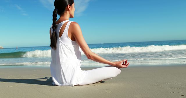 Depicts a woman in white clothes meditating on the beach, enjoying the serene ocean view. Perfect for lifestyle blogs, wellness and health websites, mindfulness and meditation apps, and travel promotions highlighting peaceful coastal experiences.