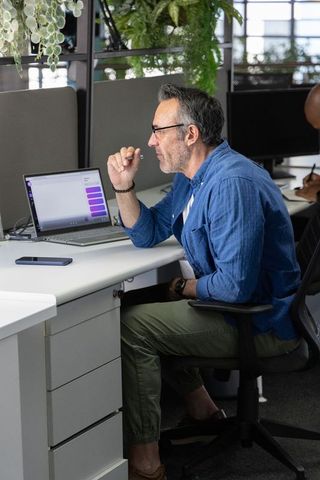 Mature professional checking laptop chat while working at modern open-plan office
