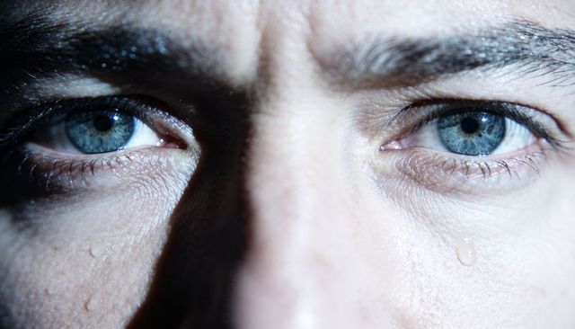 Male closeup eyes shedding tears with blue irises, skin texture and emotional intensity