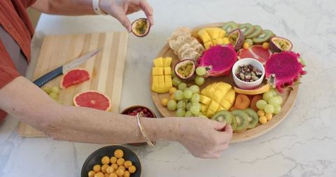 Asian senior woman arranging fruit platter with dragon fruit, mango, kiwi, passionfruit