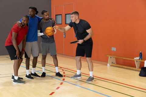 Basketball coach coaching small team on indoor court pointing at tablet during practice
