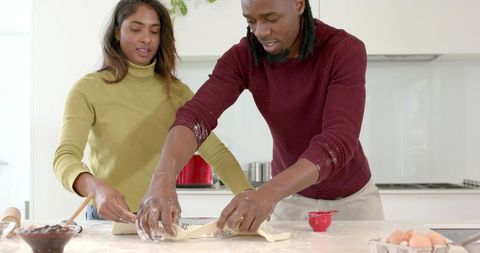 African american man and indian woman shaping pastry dough together in modern kitchen