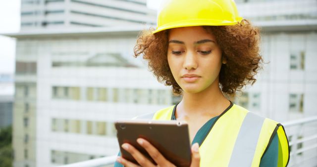 Female engineer in safety gear using digital tablet for inspection on a construction site. Ideal for content related to female professionals in engineering, modern construction practices, technology in the construction industry, urban development, and safety standards.