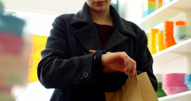 Image of a person wearing a smartwatch while holding a brown paper shopping bag. Ideal for consumer technology, retail shopping experience, and convenience-themed advertisements. Can be used for promoting shopping apps, time management tips, or retail services.