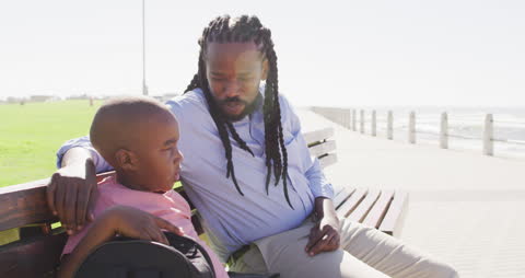 Father Sitting on Bench Talking with Son Near Seaside