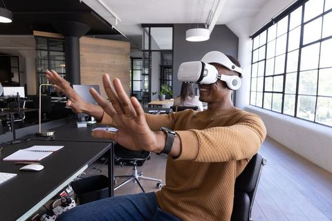 Businessman wearing VR headset engaging with virtual workspace in modern open-plan office