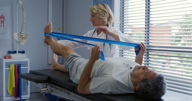 Senior man doing physical rehabilitation exercises with assistance from a female physical therapist. She uses a resistance band to help stretch and strengthen leg muscles. Ideal for concepts related to healthcare, elderly fitness, rehabilitation, and physical therapy. Can be used for medical articles, health and wellness blogs, or promotional material for physical therapy clinics.