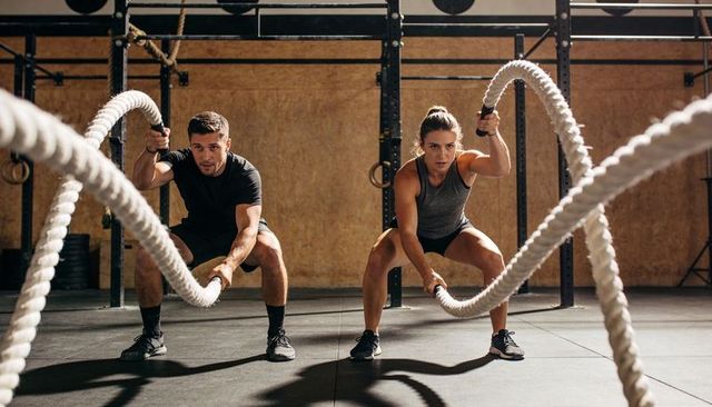 Intense battle rope training duo performing explosive full-body crossfit workout in functional gym