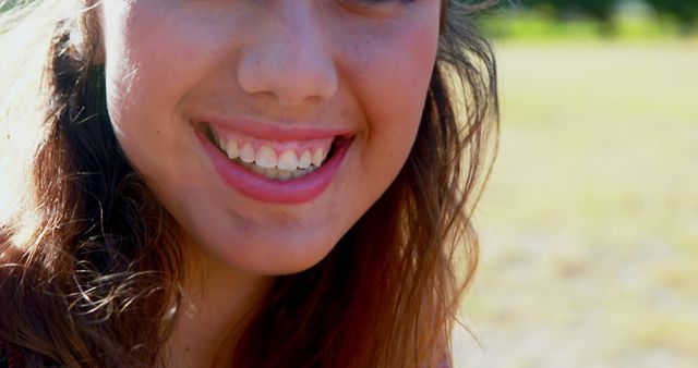 Young woman smiling outdoors under natural sunlight. Perfect for promoting dental health, happiness, and outdoor activities. Great for use in ads for lifestyle, personal care, and wellness.