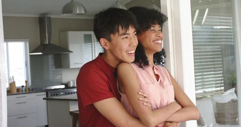 Young couple hugging and smiling in bright modern kitchen doorway, warm domestic moment