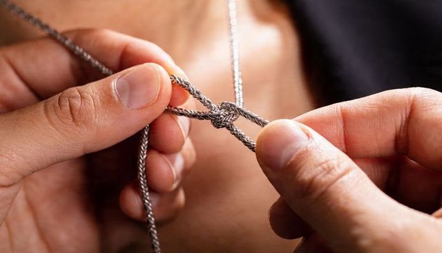 Man tying braided silver necklace knot at bare chest closeup showing hands and fingernails