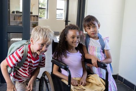 Smiling diverse schoolchildren with wheelchair and backpacks promoting school inclusion