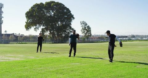 Men practicing baseball drill on sunny grassy field wearing caps and gloves