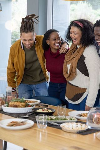 Friends laughing around festive dining table with roast chicken and holiday dishes