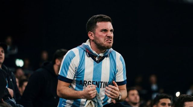 Grimacing argentina fan clenching fists and holding scarf during intense stadium moment