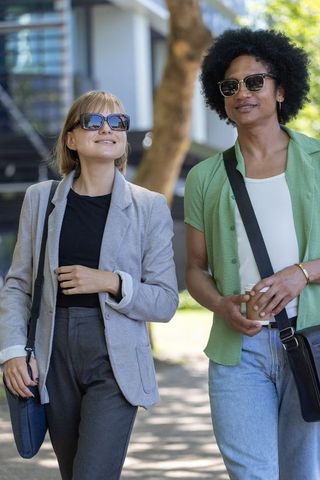 Diverse friends walking pathway wearing sunglasses carrying coffee and crossbody bags