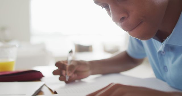 Young boy concentrating on writing notes at home, emphasizing diligent studying and focus. This can be used in educational materials, advertisements for learning tools, or articles promoting study habits and academic focus.