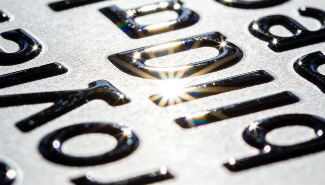 Glossy embossed letters catching sunlight on textured metal plaque with starburst flare