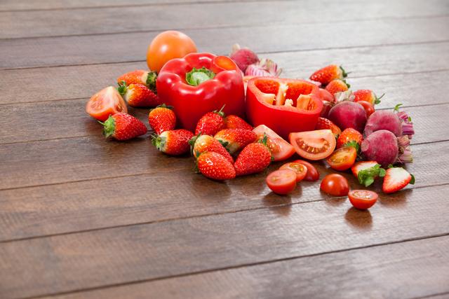 Various fresh vegetables and fruits, including strawberries, tomatoes, and red peppers, are arranged on a wooden table. This vibrant and colorful arrangement emphasizes healthy eating and dietary concepts. Ideal for use in nutritional blogs, healthy lifestyle websites, and promotional materials for organic food markets.