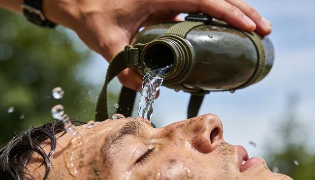 Pouring water over dusty face from olive-green canteen during outdoor hike