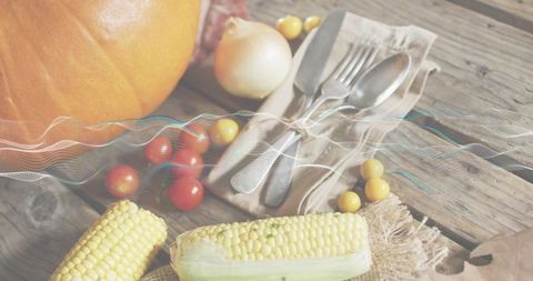 Rustic harvest table featuring corn cobs, pumpkin, cherry tomatoes and tied silverware