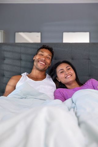 Smiling Couple Relaxing in Bed Under White Duvet in Modern Bedroom