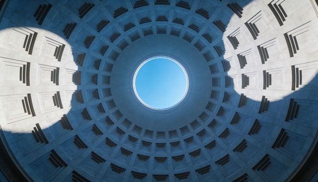 Concentric coffered dome with central oculus revealing bright blue sky and shadows
