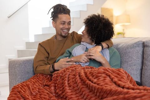Couple cuddling on sofa sharing cozy rust throw and warm conversation